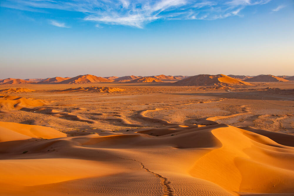 A camel caravan moving across large, orange desert dunes